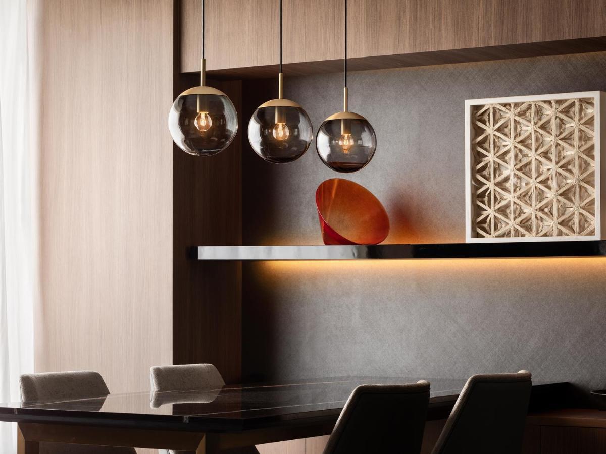 Mitsui Garden Hotel Roppongi Tokyo Premier Exteriör bild The photo depicts a modern interior design scene. It features a sleek dining area with a dark wooden table and comfortable chairs. Above the table, there are three pendant lights with glass shades that provide ambient lighting. A geometric art piece 