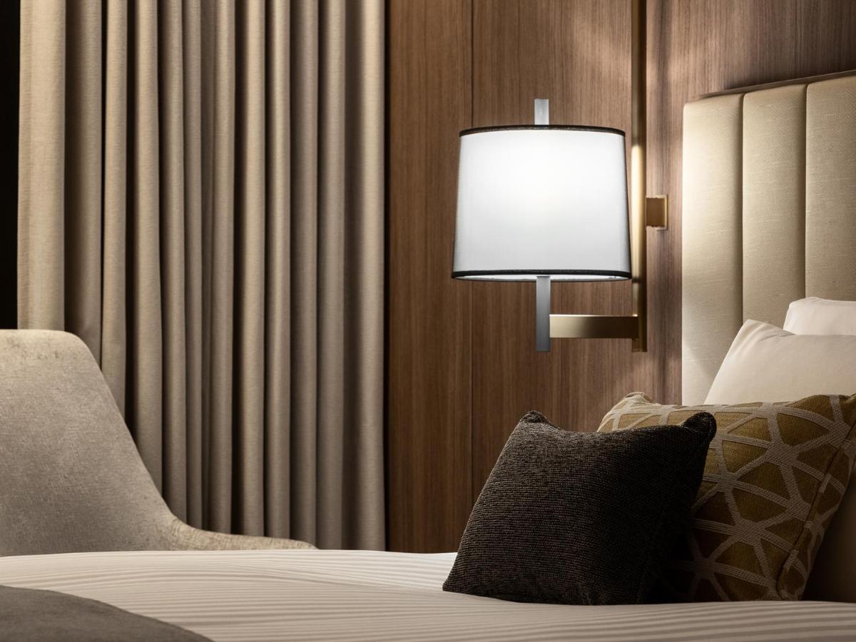 Mitsui Garden Hotel Roppongi Tokyo Premier Exteriör bild The photo displays a cozy hotel room setting. It features a neatly made bed with white linens and several decorative pillows. To the side, there’s a stylish bedside lamp mounted on the wall with a round white shade. Behind the lamp, there are elegant