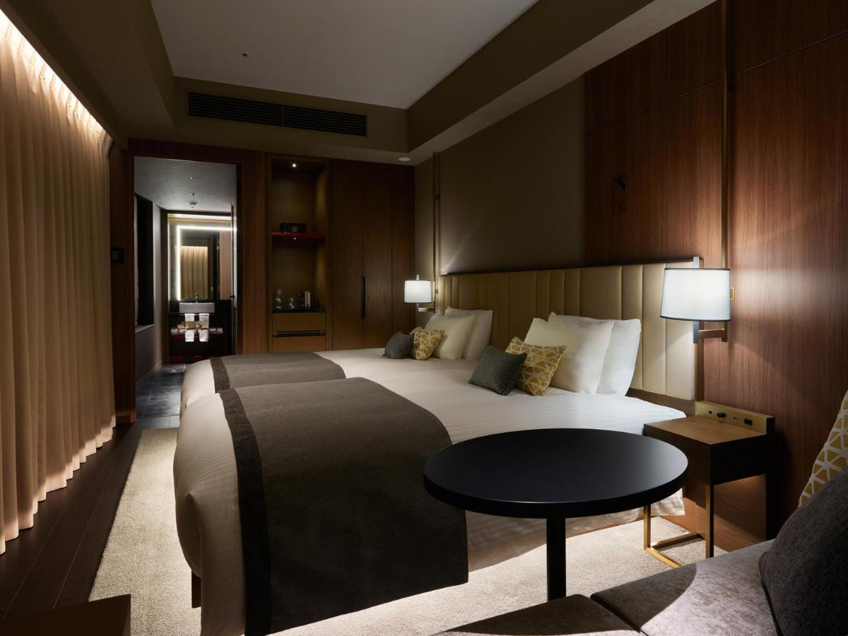 Mitsui Garden Hotel Roppongi Tokyo Premier Exteriör bild The photo shows a stylish hotel room featuring two beds with plush bedding and decorative pillows. The walls are made of wood, creating a warm and modern atmosphere. There are bedside lamps on each side of the beds providing soft lighting. A small ro