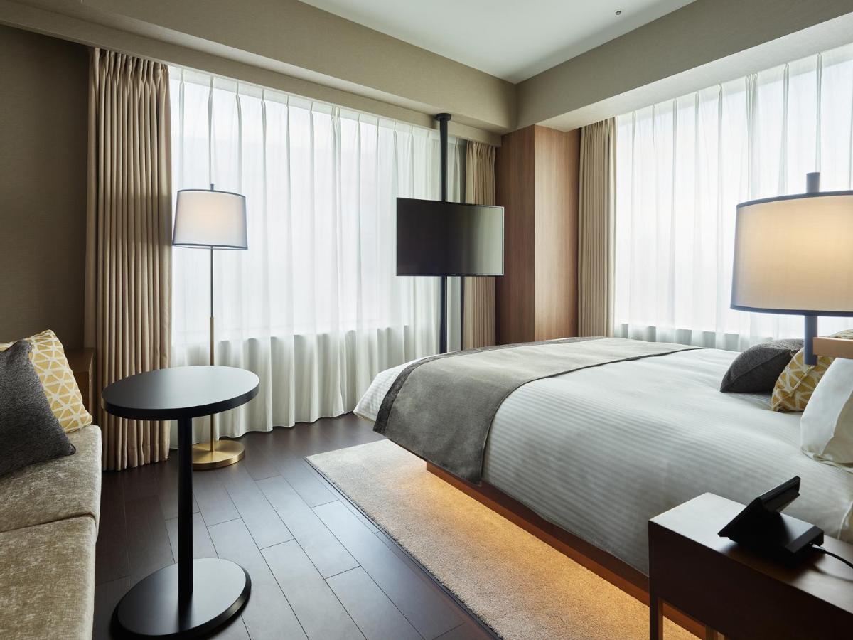 Mitsui Garden Hotel Roppongi Tokyo Premier Exteriör bild The photo shows a modern hotel room with a contemporary design. It features a large bed with crisp white linens, sitting against a wall with floor-to-ceiling windows covered by sheer curtains, allowing natural light to filter in. To the side, there's