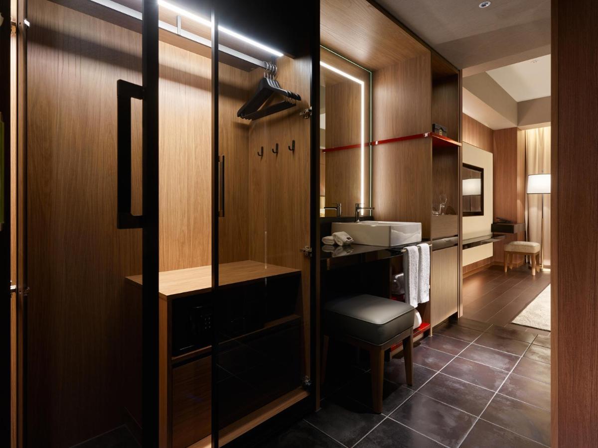 Mitsui Garden Hotel Roppongi Tokyo Premier Exteriör bild The photo depicts a modern and stylish hotel room's closet area. It features wooden cabinetry with a sleek finish, including mirrored doors. Inside, there are hangers for clothing and hooks mounted on the wall. A small bench or chair is positioned ne