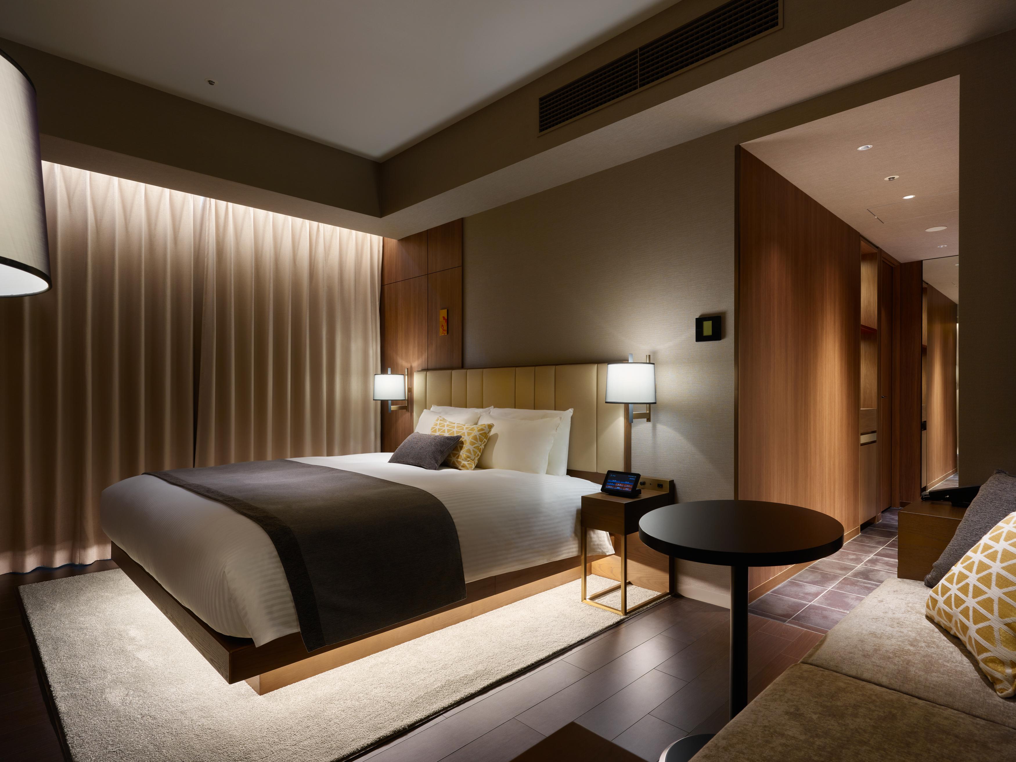 Mitsui Garden Hotel Roppongi Tokyo Premier Exteriör bild The photo shows a modern hotel room featuring a king-sized bed with neutral-colored bedding and accent pillows. There are two bedside lamps on either side of the bed, providing a warm glow. The walls have a wood finish, and there's a soft area rug on