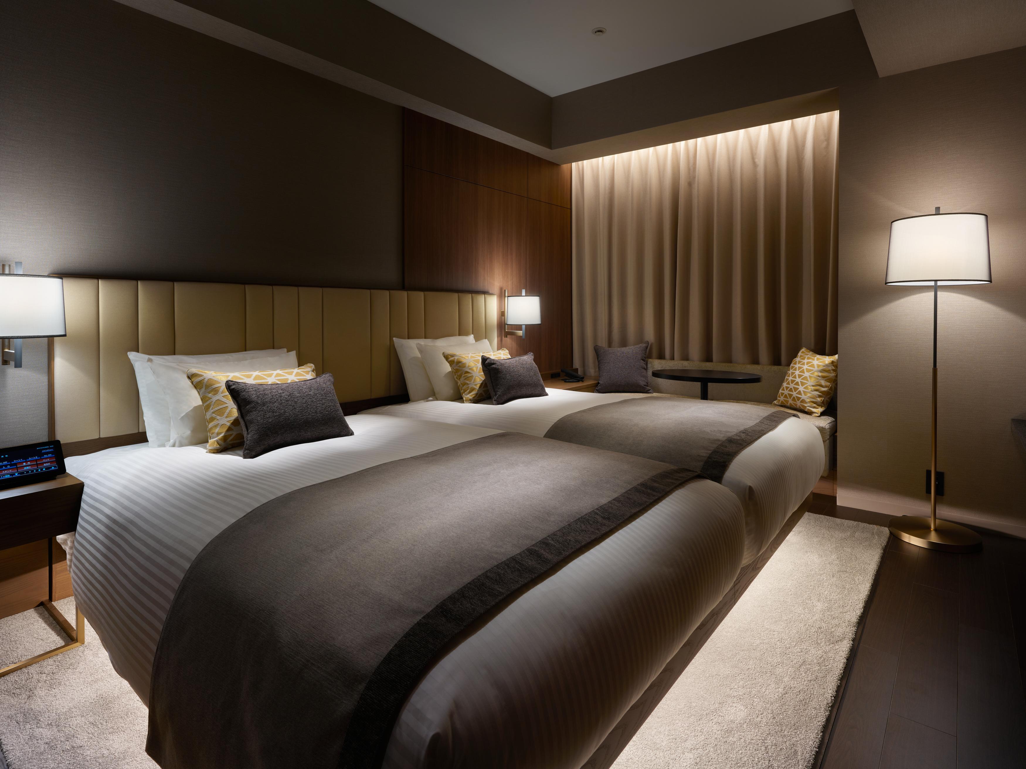 Mitsui Garden Hotel Roppongi Tokyo Premier Exteriör bild The photo shows a modern hotel room featuring two beds with elegant bedding in neutral colors. Each bed is adorned with decorative pillows. The room has a sophisticated ambiance with dim lighting, highlighted by table lamps on either side of the beds