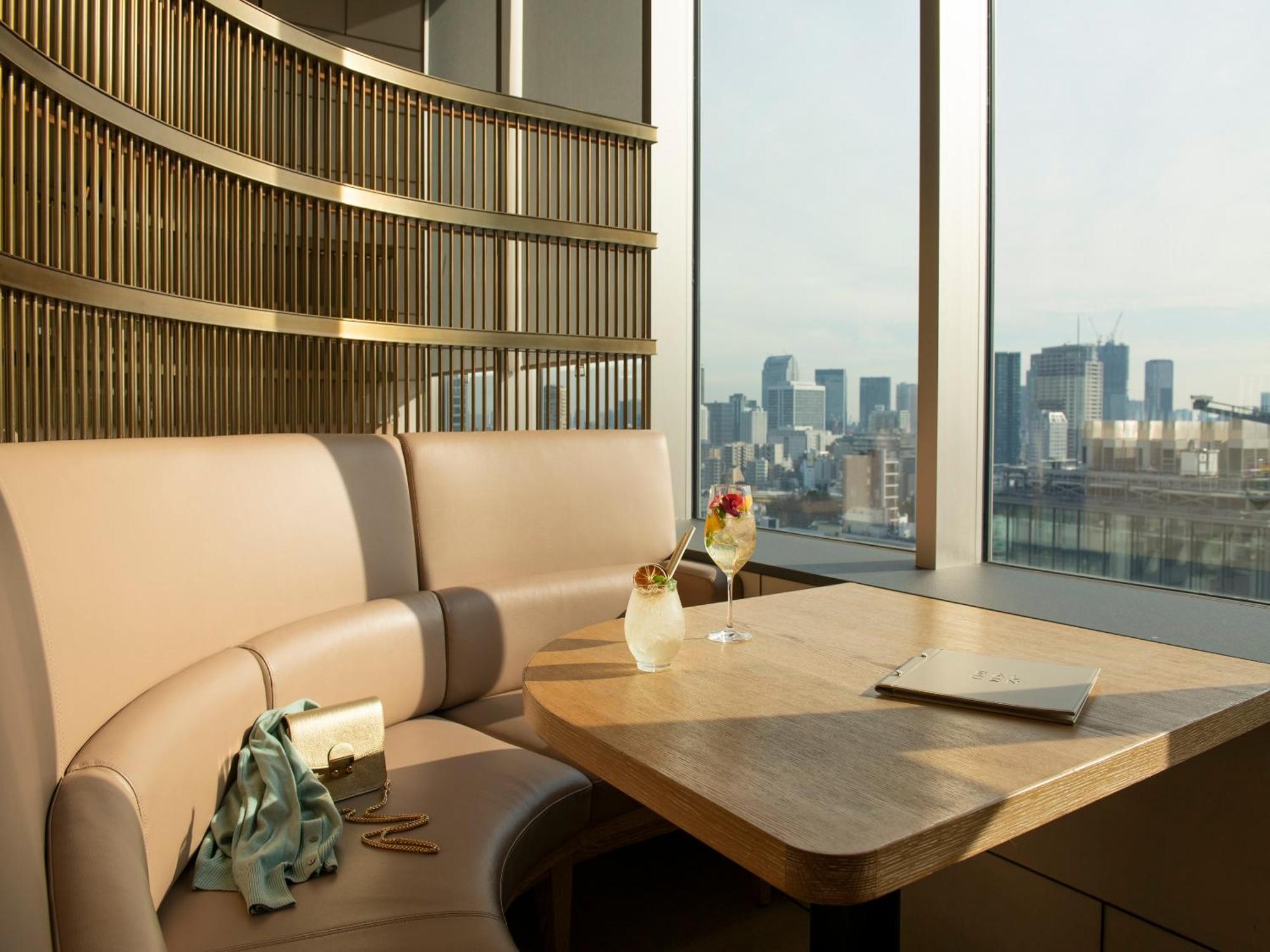 Mitsui Garden Hotel Roppongi Tokyo Premier Exteriör bild The photo depicts a cozy, modern seating area with a curved booth that features soft, pale upholstery. A wooden table is positioned in front of the booth, and on the table, there are two elegant drinks garnished with fruit. The setting has large wind