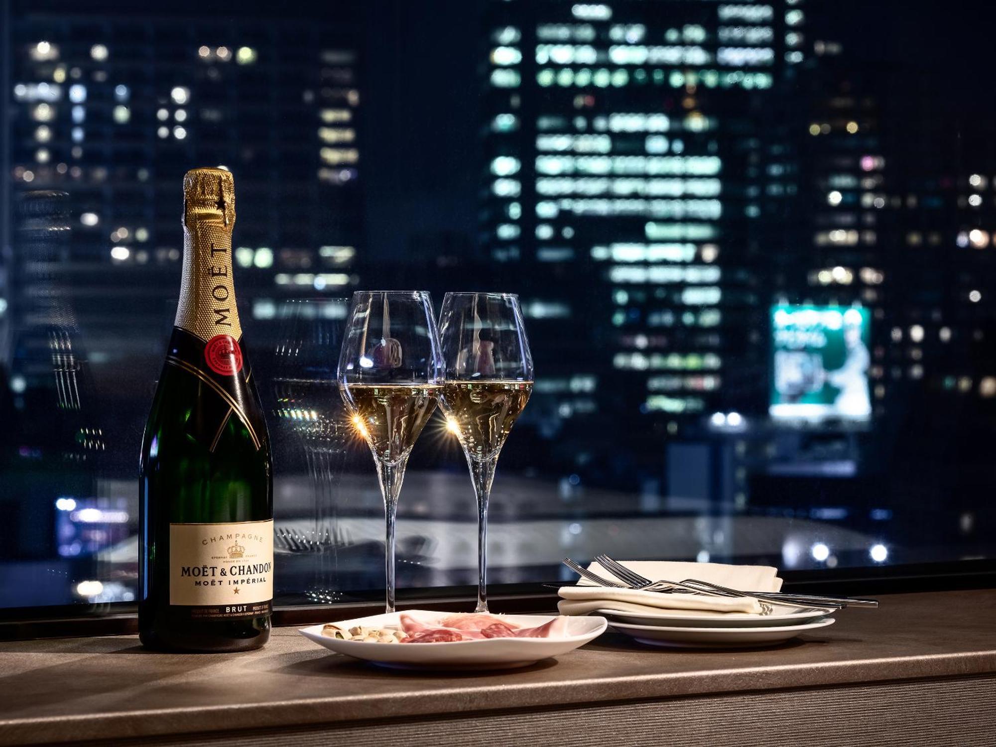 Mitsui Garden Hotel Roppongi Tokyo Premier Exteriör bild The photo features a bottle of champagne, specifically Moët & Chandon, alongside two filled champagne glasses. The table setting includes a small plate with a selection of food and neatly arranged utensils. In the background, there is a view of a cit