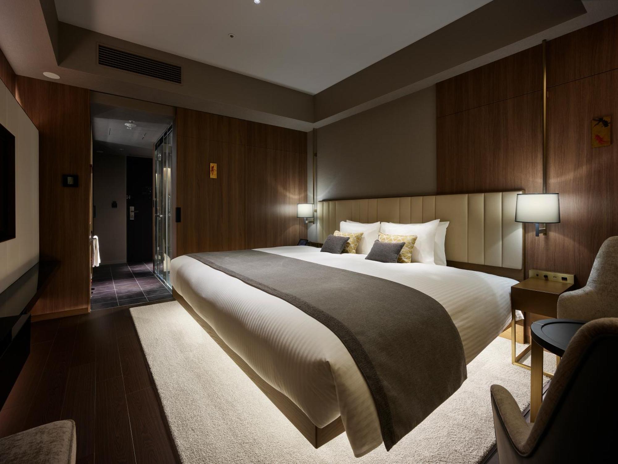 Mitsui Garden Hotel Roppongi Tokyo Premier Exteriör bild The photo shows a modern hotel room featuring a large bed with a neutral-colored duvet and a dark throw blanket. The headboard is upholstered, and there are two bedside lamps on either side of the bed. The walls have a warm wood paneling, contributin
