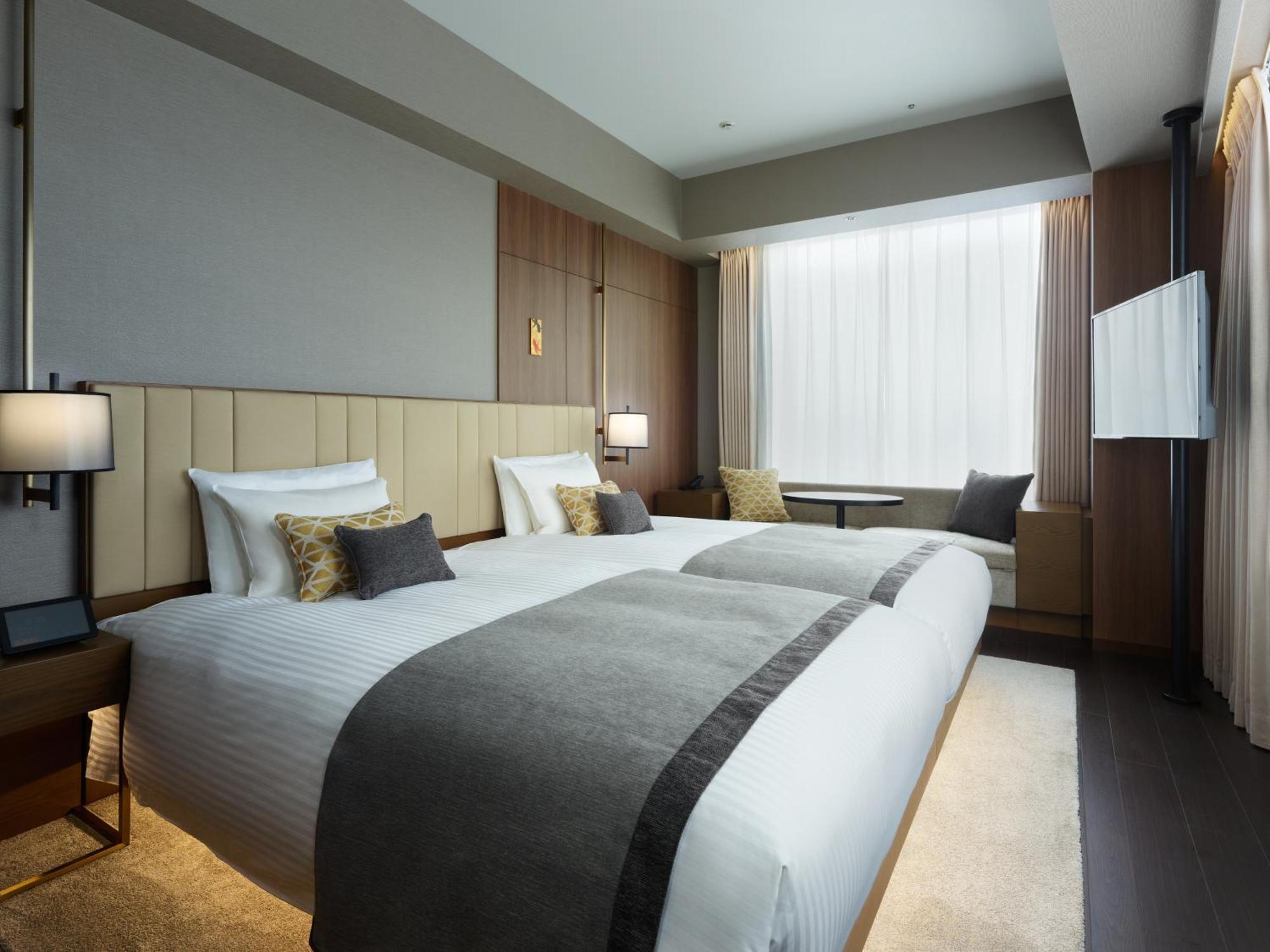 Mitsui Garden Hotel Roppongi Tokyo Premier Exteriör bild The photo shows a modern hotel room featuring two beds with white linens and decorative pillows. The room has a minimalist design, with neutral-colored walls and wooden accents. Natural light comes in through large windows, which are partially covere
