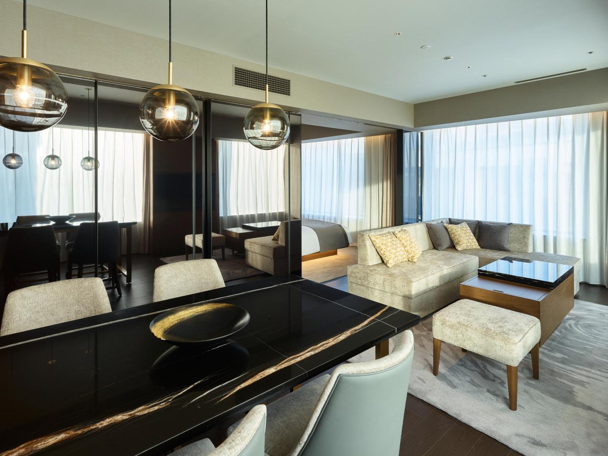 Mitsui Garden Hotel Roppongi Tokyo Premier Exteriör bild The photo shows a modern and stylish living area. It features a dining table with elegant chairs, a comfortable seating area with a light-colored sofa, and a coffee table. The room is well-lit by large windows draped with sheer curtains, allowing nat
