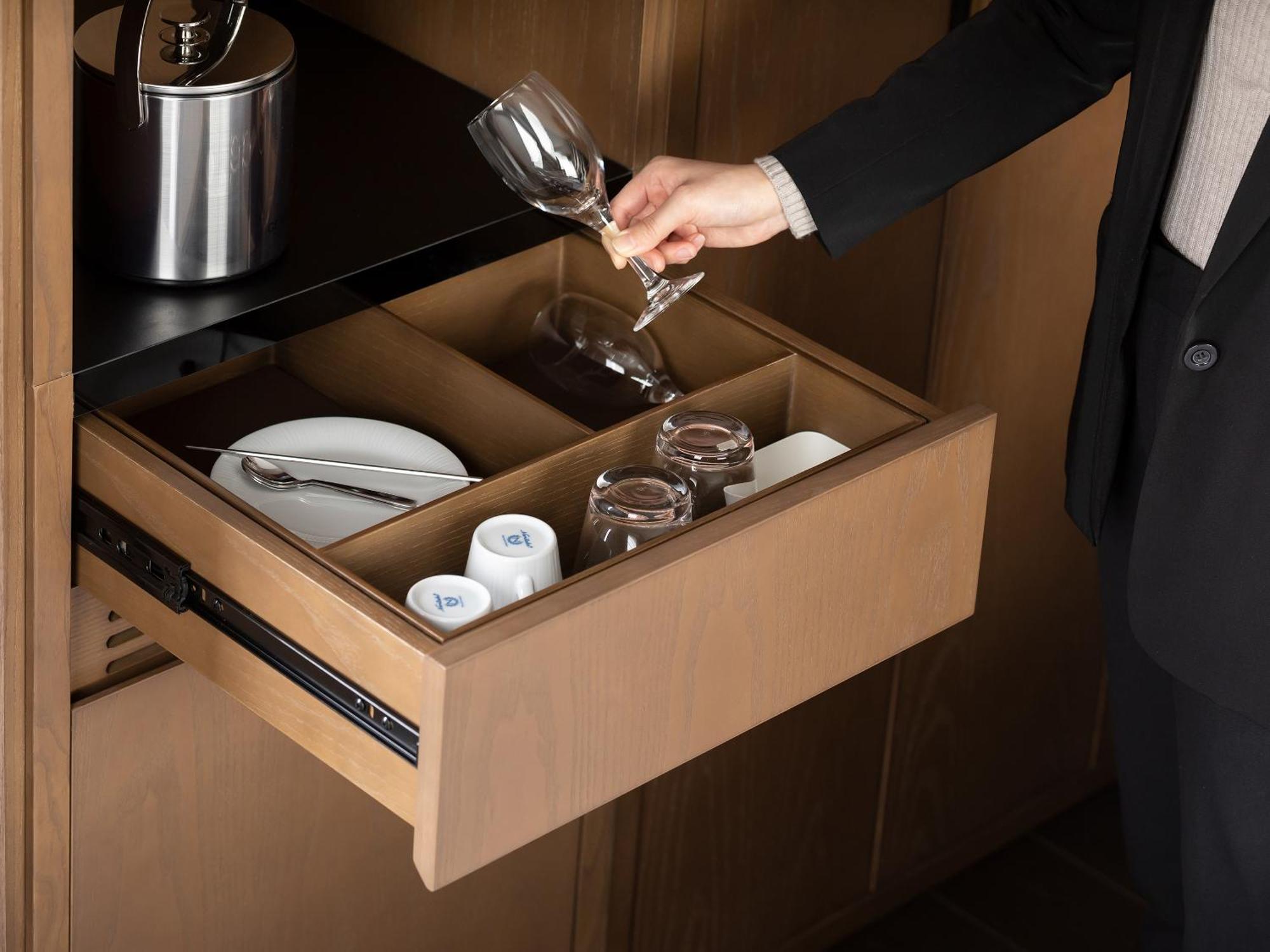 Mitsui Garden Hotel Roppongi Tokyo Premier Exteriör bild The photo depicts a wooden kitchen drawer being pulled open, revealing a neatly organized selection of dishware. Inside, there are glass cups, a wine glass being held by a person, and plates. The setting appears modern and sleek, with a sophisticated