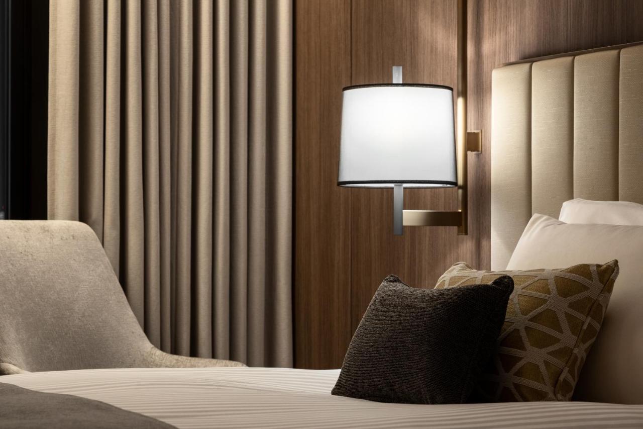 Mitsui Garden Hotel Roppongi Tokyo Premier Exteriör bild The photo shows a cozy hotel bedroom setting. There is a neatly made bed with white linens and a few decorative pillows, including a dark one and another with a geometric pattern. To the side, there is a soft armchair and a modern wall lamp mounted a